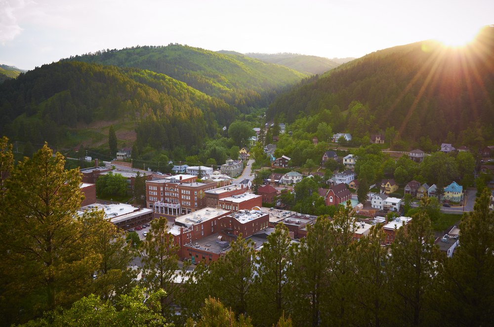An aerial view of the city of Deadwood in a valley in South Dakota with sun setting behind one of the hills