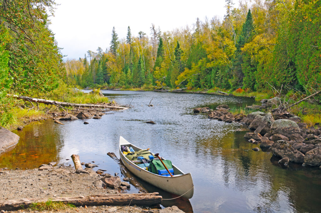 fully stocked canoe on river's edge with trees on both sides of the river exploding with the colors of fall in MN.