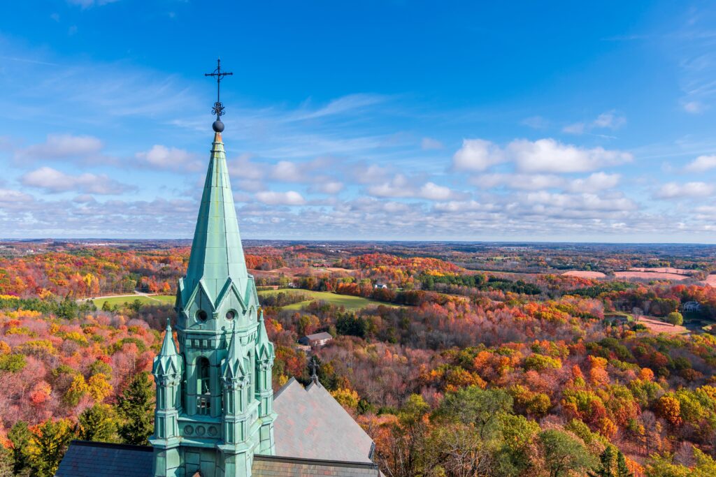 Green spired tower jutting into sky surrounded by brilliant Wisconsin fall foliage.