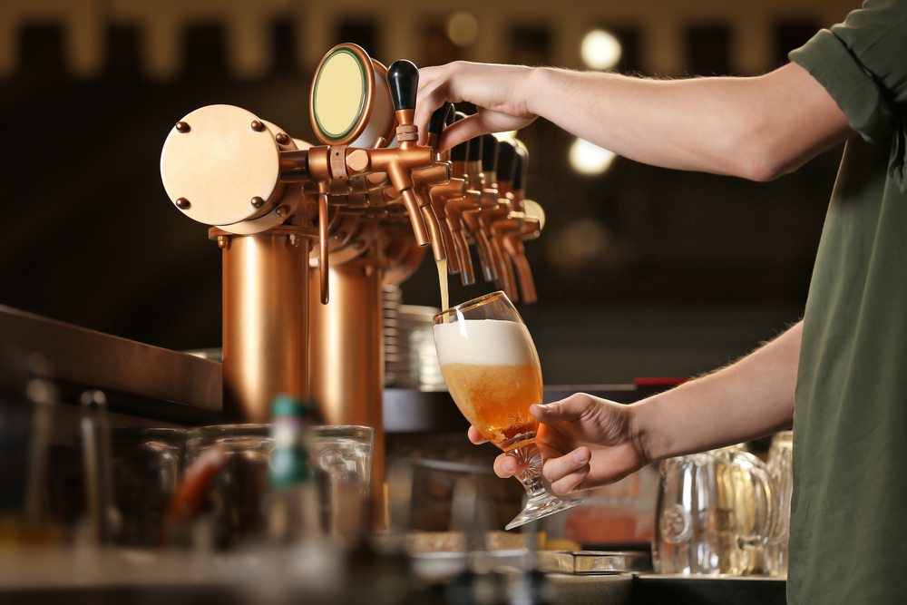 A fancy copper beer tap with someone pouring a light colored beer out of one of the taps at one of the breweries in Chicago.