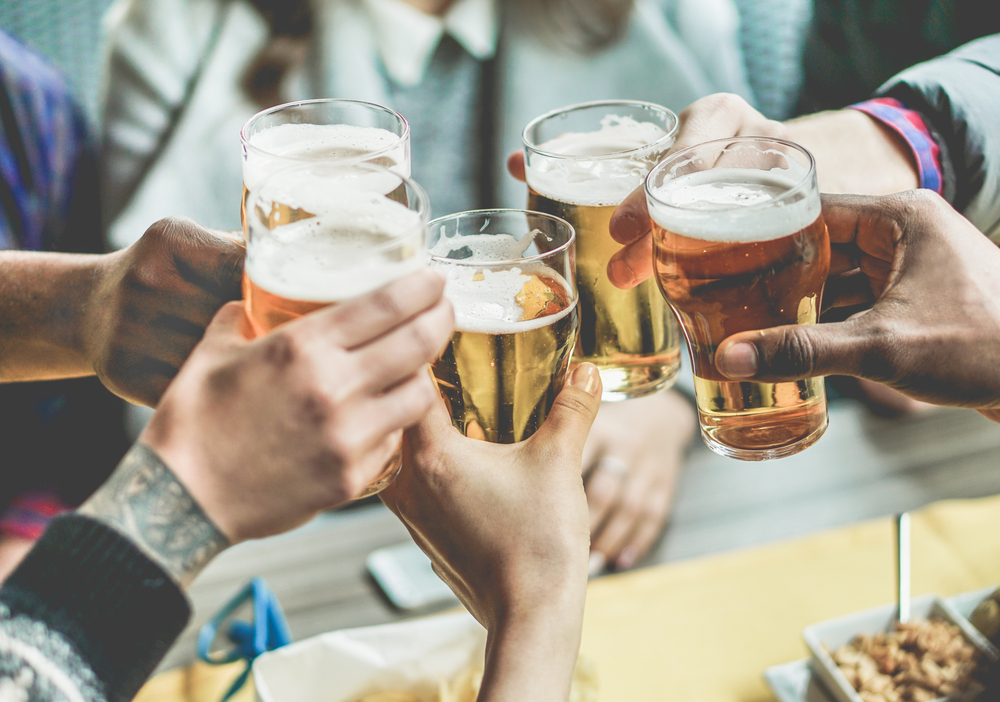 A group of hands clinking their small glasses of a light colored beer together at one of the breweries in Chicago!