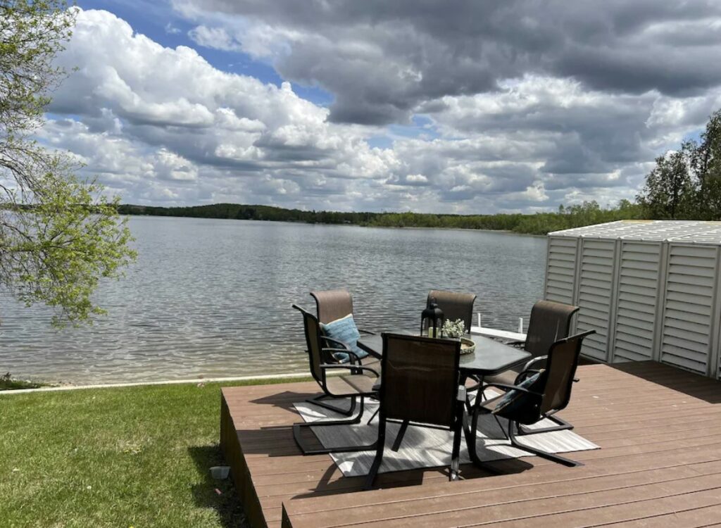 The deck of a cabins in North Dakota looking out onto a lake with seating, and some grassy areas