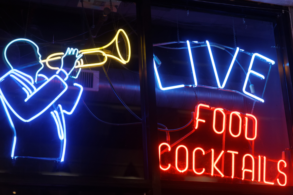 A neon sign with a man playing the trumpet and the words 'Live' and 'Food Cocktails' in blue and red. 
