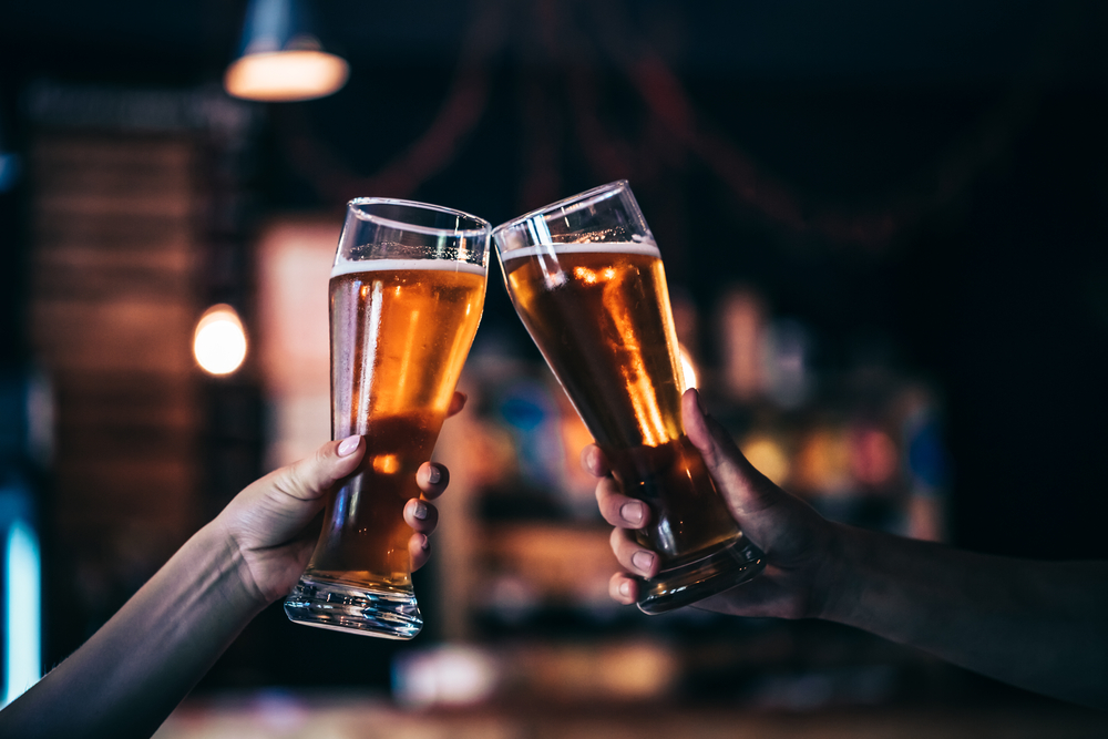 Two hands clinking glasses of beer together