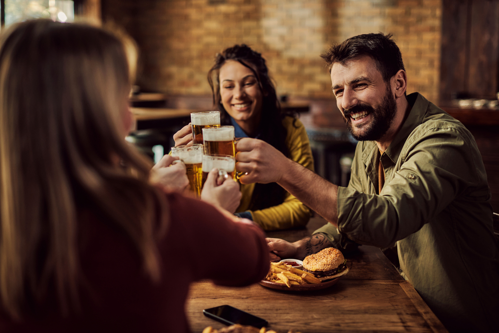 A group of people sitting at a table in a breweries in Chicago, holding up their beer glasses, and enjoying burgers. 