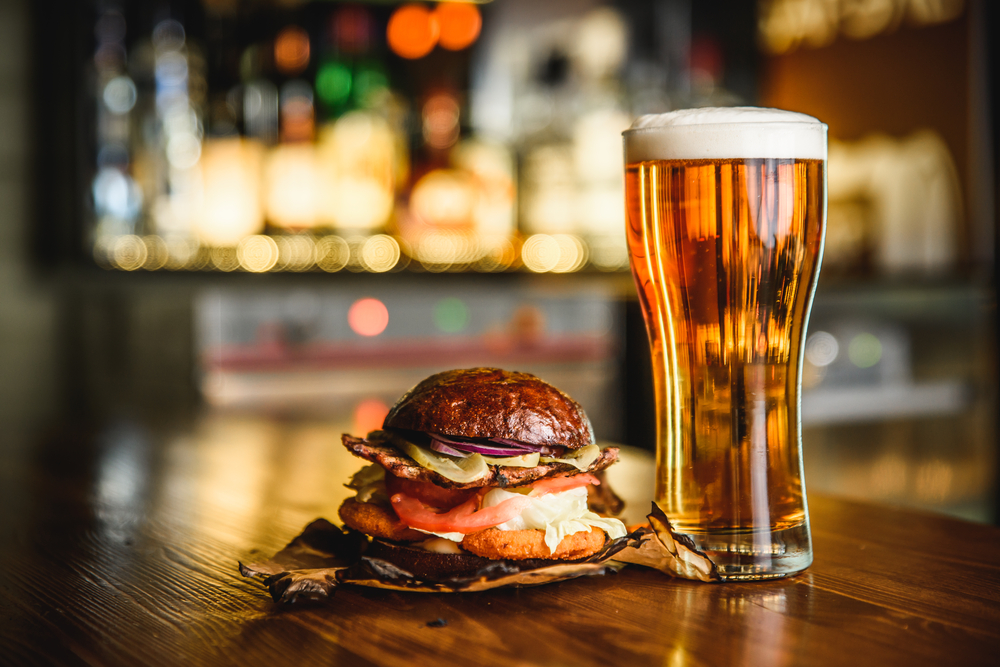 Burger in bun on table with glass of light beet at a restaurant in Akron