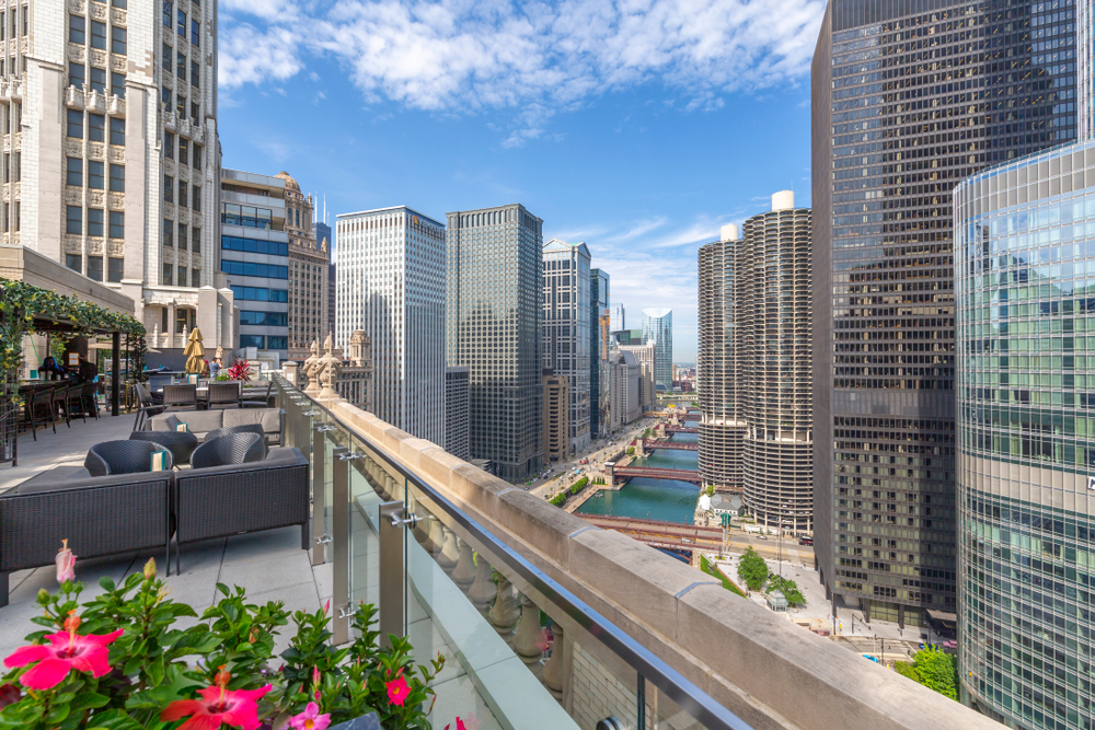 A view of the Chicago River from a rooftop bar with seating, flowers, and a bar on a sunny day