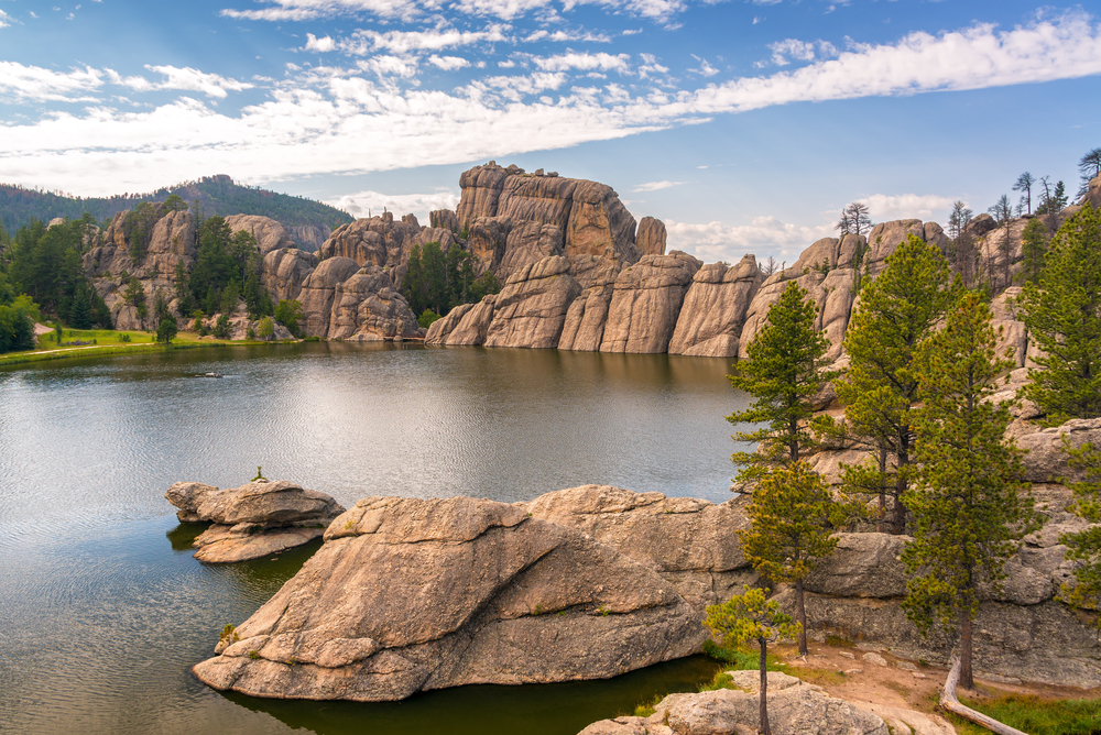 A view of Sylvan Lake, surrounded by rock formations and tall trees, on a sunny day. 