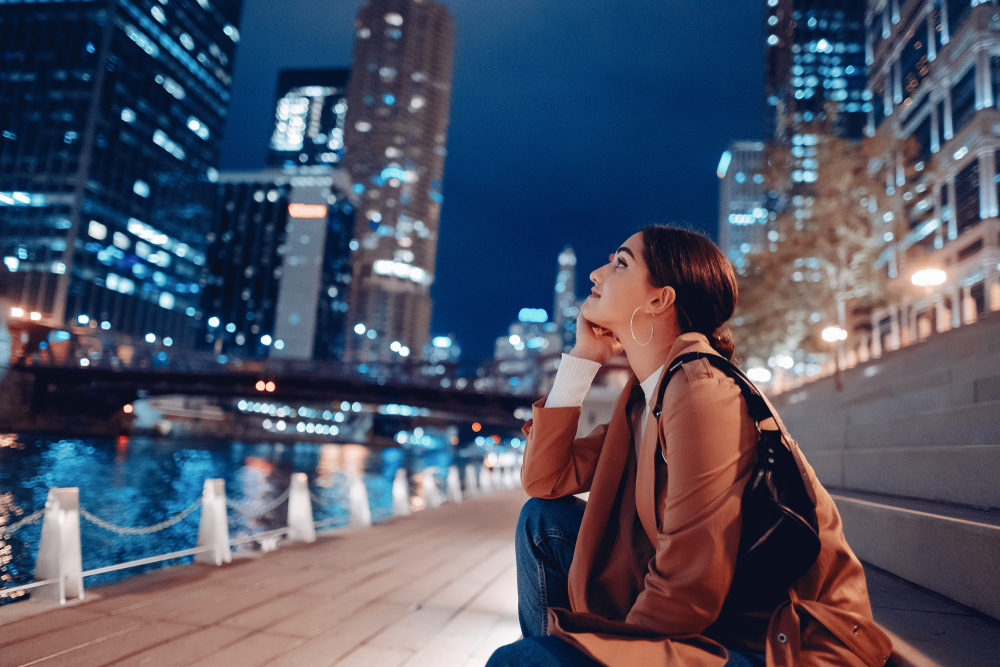 A woman sitting on the Chicago Riverwalk looking at the skyline all lit up, one of the best things to do in Chicago at night