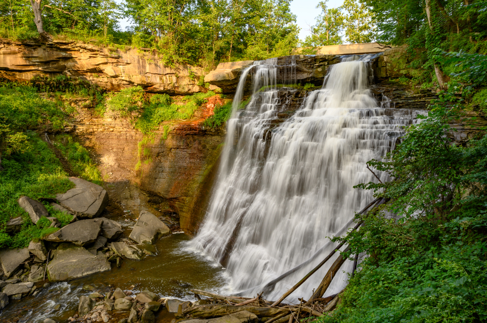 Brandywine Falls in Cuyahoga Valley National Park, Ohio at Dusk in Summer. The falls cascade over the rocks and their is foilage in the foreground. 