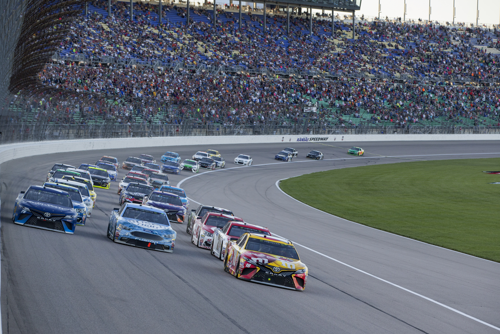 Racecars on round cement course with spectators in background.