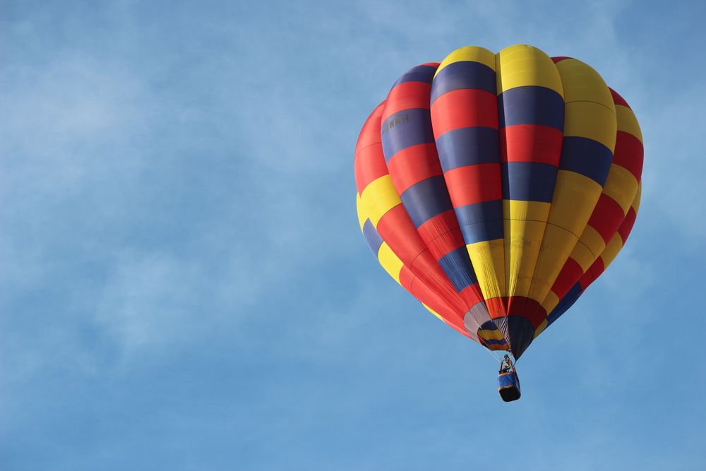 A balloon flying in the sky. The balloon is multi-coloured 