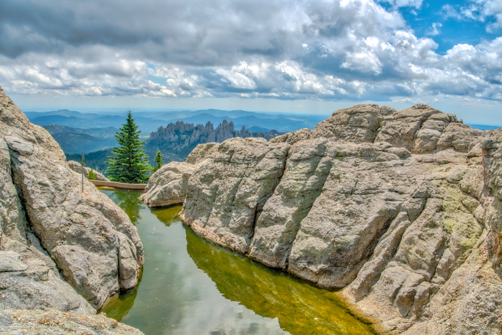 Black Elk Peak at Custer State Park in South Dakota Black Hills Area. Rocks and lakes are in the foreground and the  view below is of trees and rocks. 