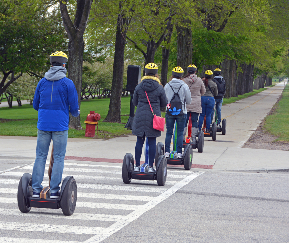 Beginner Segway riders taking a tour of some of the many parks in Chicago. They are in a line all wearing helmets 