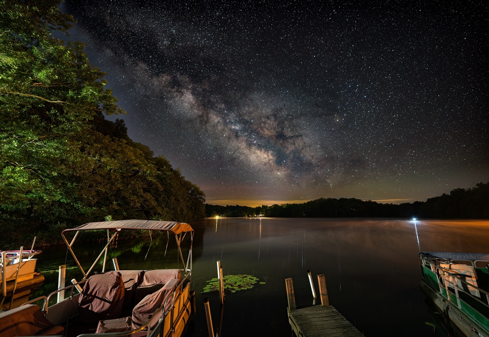 Night photo of the milky way over Logan Lake with boats in the foreground.