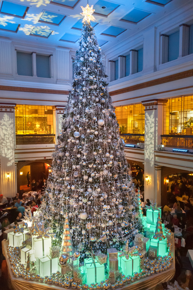 Tall silver decorated Christmas tree surrounded by presents in the Walnut Room at Macy's.