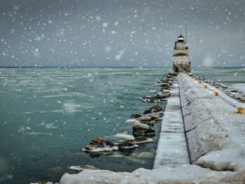 Snowflakes falling on a pier with a lighthouse