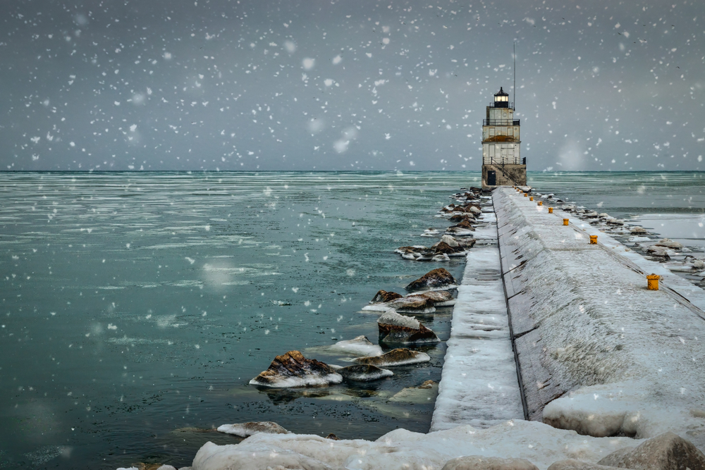 Snowflakes falling on a pier with a lighthouse