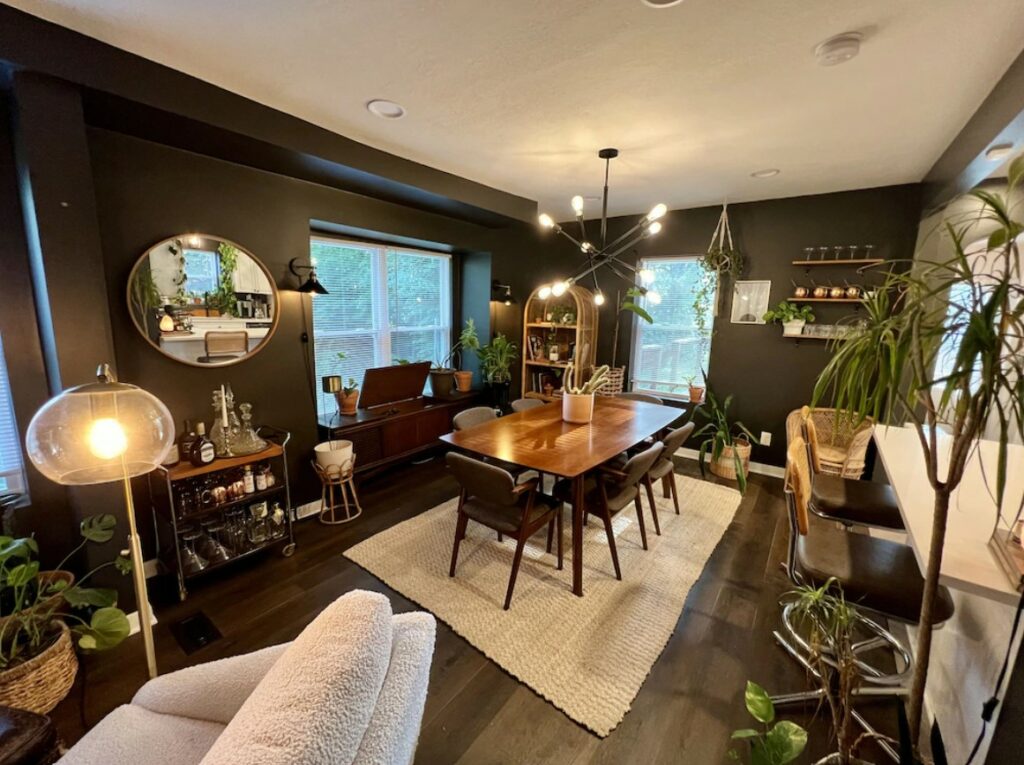 A dining room with dark walls, wood floors, and lots of green plants everywhere