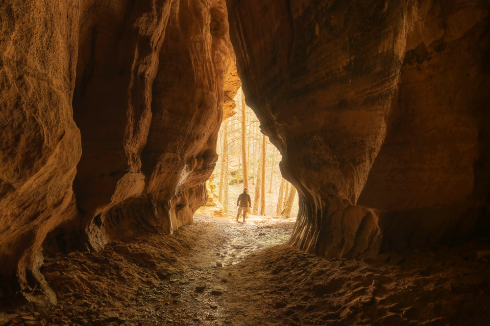 Looking at the chapel window shaped opening from inside a cave with a person standing in the opening. One of the best caves in Ohio.