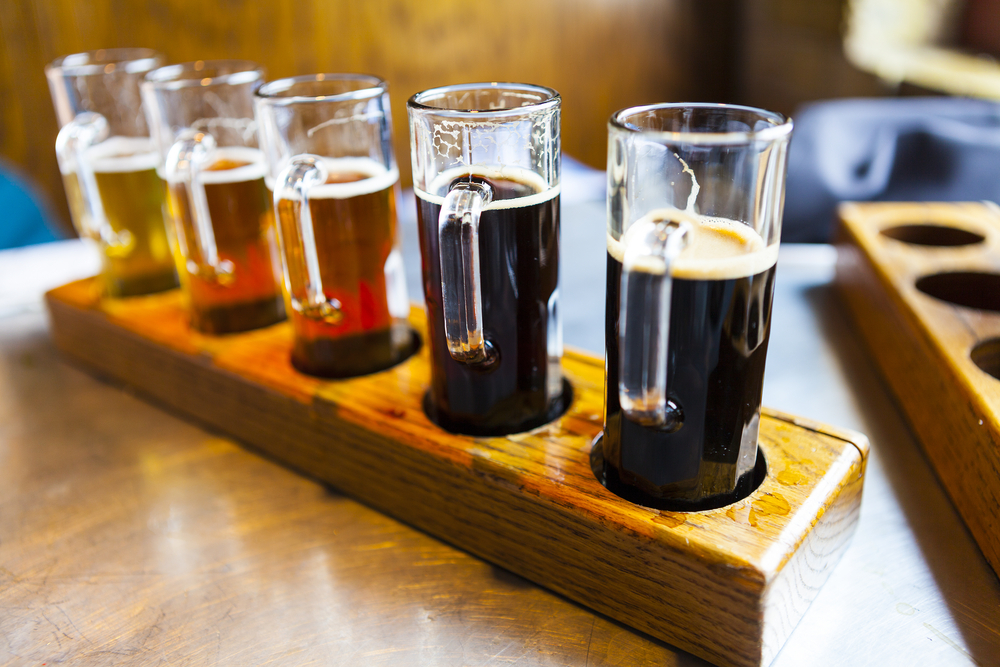 A flight of craft brews ranging from light to dark in color in a wooden beer flight holder
