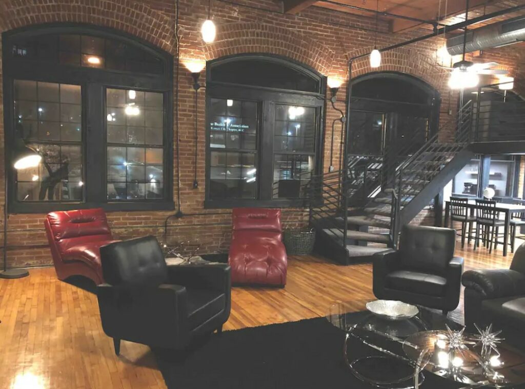 An industrial loft with red leather chairs, black leather chairs, huge windows, exposed brick walls, and a metal staircase one of the best airbnbs in Kansas City Missouri