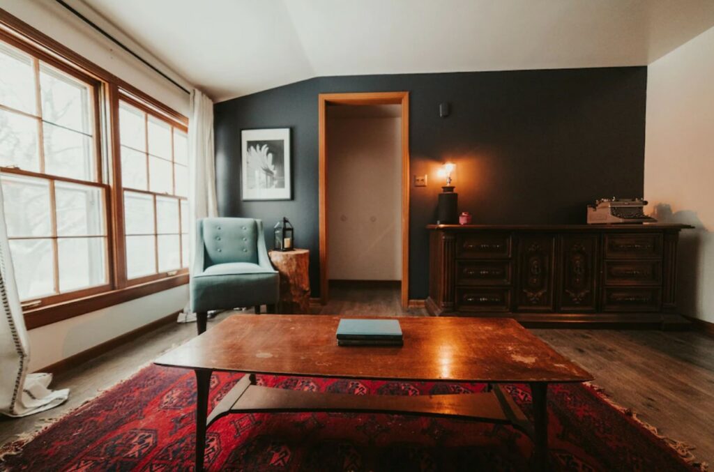 The living room of one of the best airbnbs in Kansas City Missouri with a dark wall, wood floors, seating, a red rug, and large windows