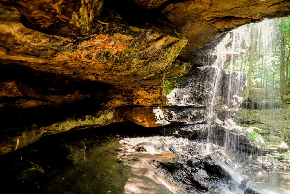 A small narrow cave hidden behind a waterfall in the woods