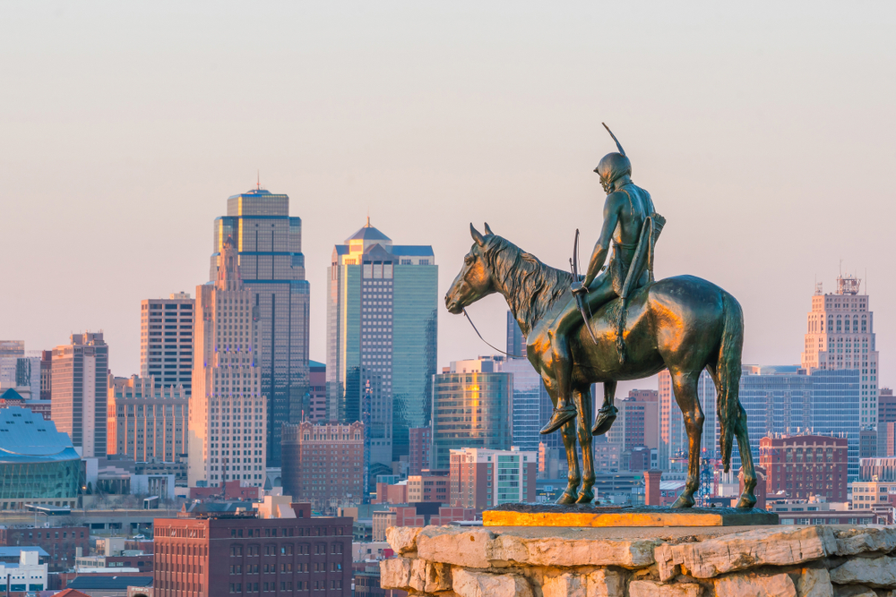 A statue of a Native American riding a horse looking out onto the skyline of Kansas City Missouri
