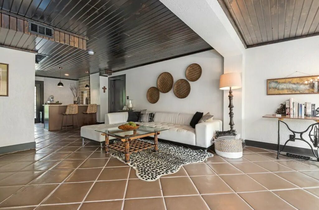 A spacious living area with white walls, tile floors, dark wood ceilings, and a large white sectional. 
