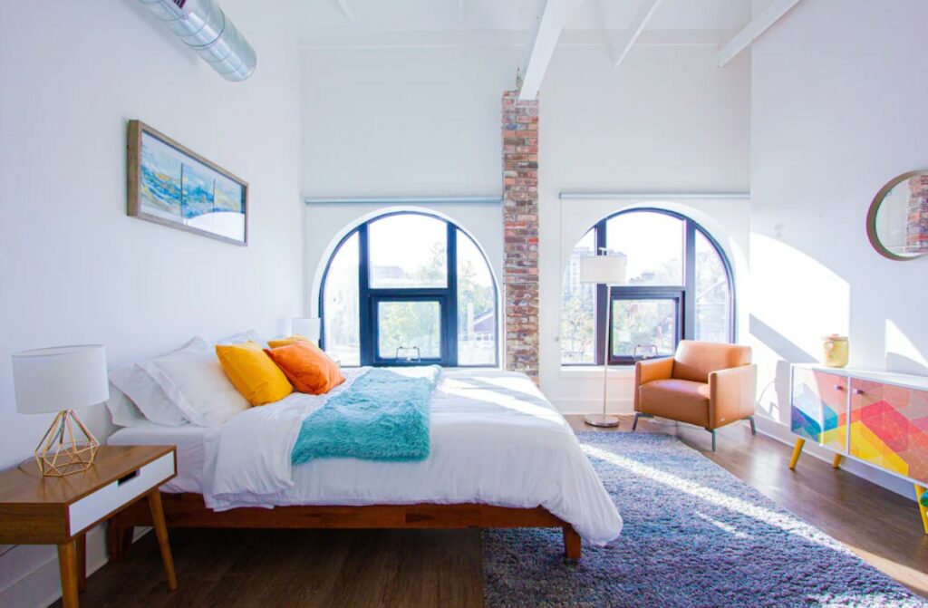 A bright and modern airbnbs in Kansas City Missouri with semi-circle windows, bright white and exposed brick walls, and colorful decor
