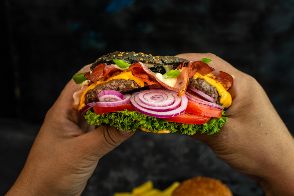 Person with  juicy fresh cheesburger in his hands. The hamburger is full of onions and tomatoes. 