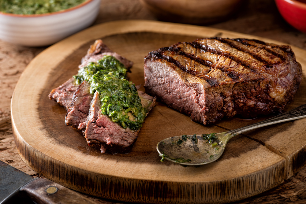 A delicious medium rare fire grilled argentina style steak with chimichurri verde sauce. It is on a wooden block