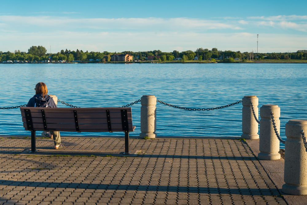 A person sitting on a bench at the Rotary Island Park, one of the best things to do in Sault Ste Marie, looking out at the Saint Mary's River