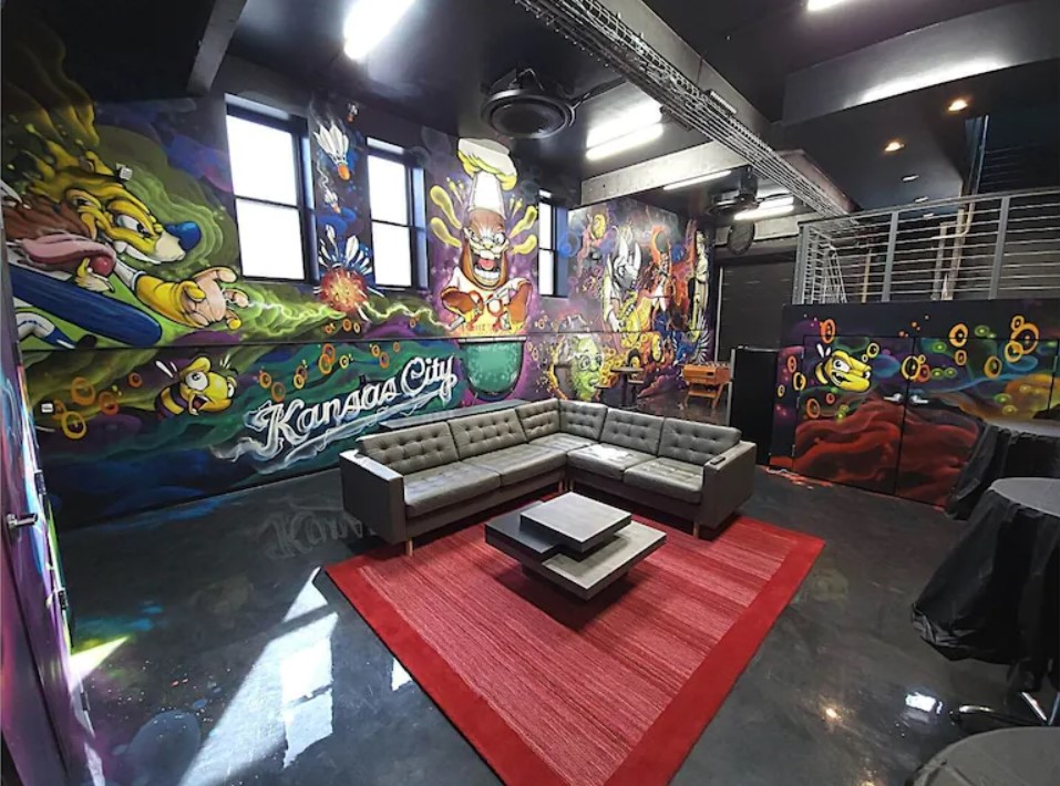 An industrial looking room with huge colorful pieces of graffiti on the walls. 