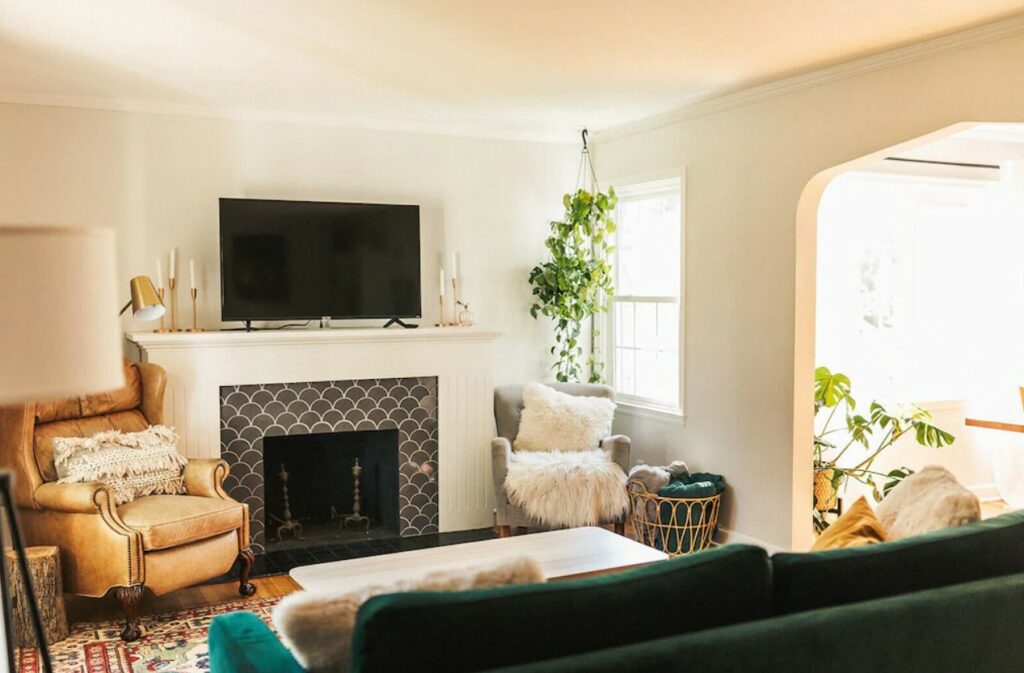 A living room with a tile fireplace, leather seats, and a green velvet sofa and plants