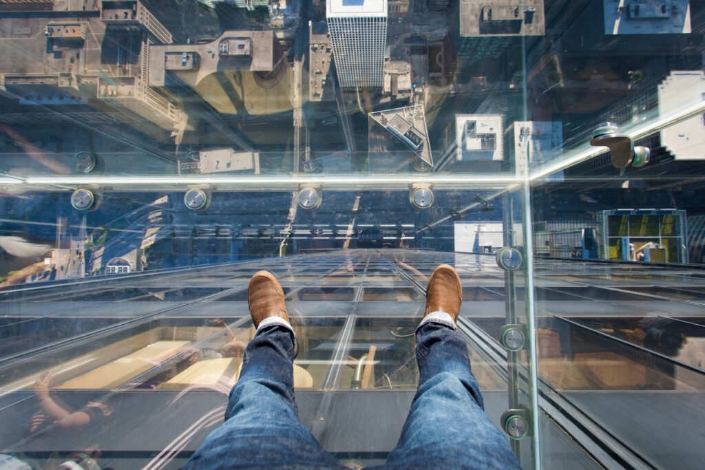 Glass floor high above street with with person wearing jeans and brown boots standing. attractions in Illinois.