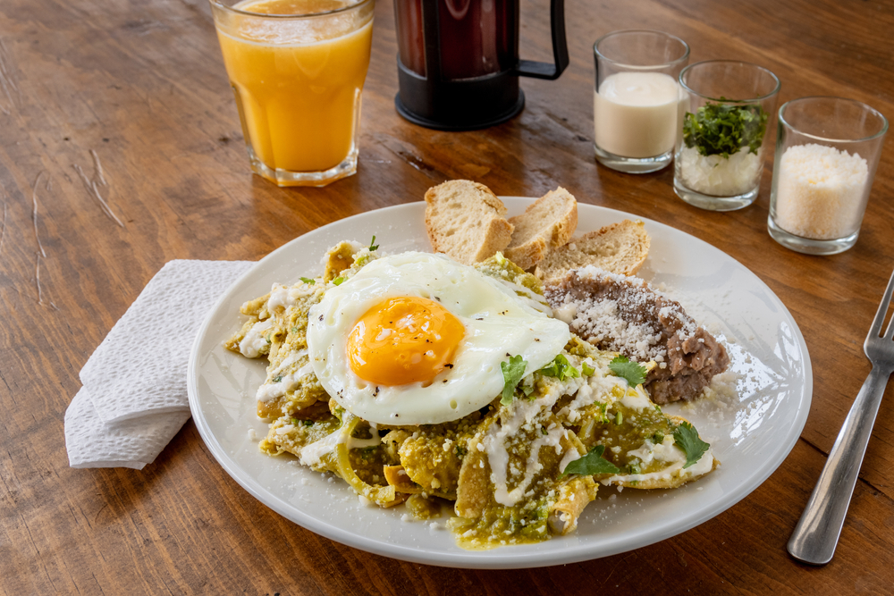 chilaquiles with eggs served on a white plate along with a yellow colored drink brunch in chicago