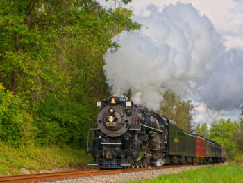 Black locomotive steaming down tracks with greenery around it during a train ride in Ohio