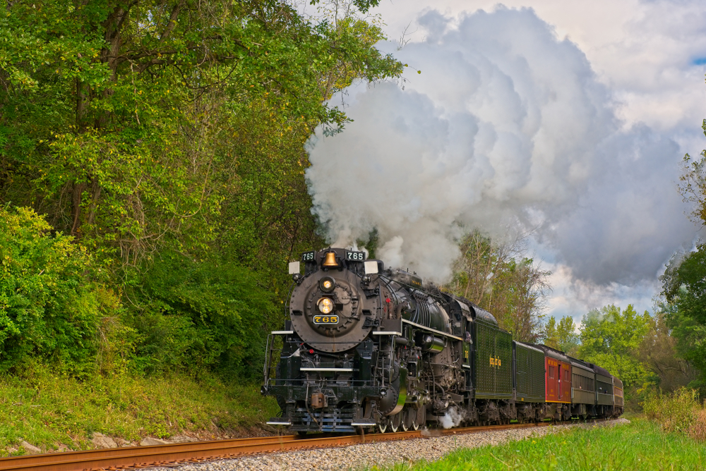 A vintage steam train spewing steam as it travels through woods.