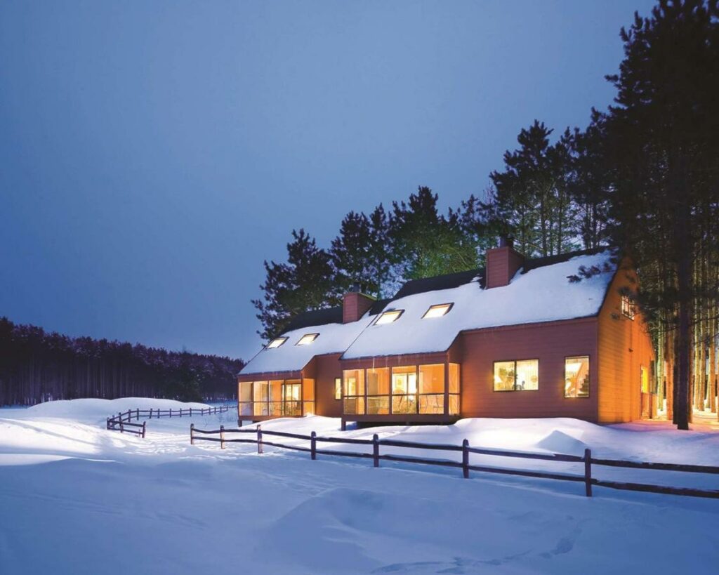 A large cabin with lots of windows covered in snow on the edge of a forest one of the best resorts in Wisconsin