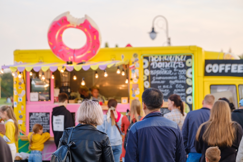 A group of people outside of a bright yellow and pink donut food truck