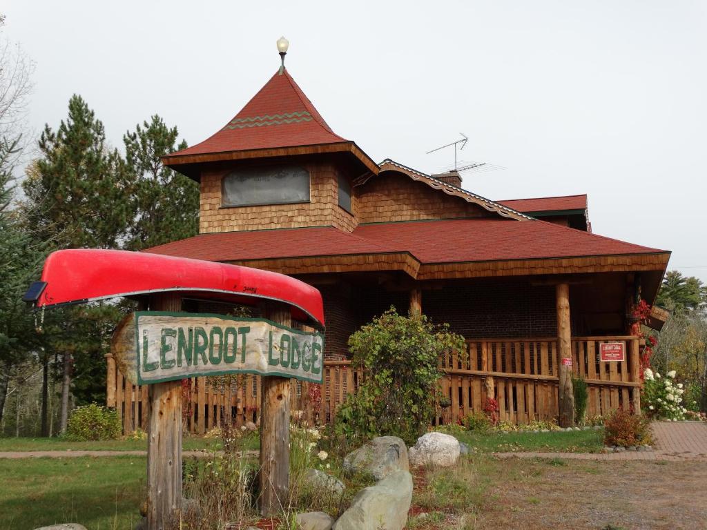 The front of a large log cabin structure with a sign out front that says 'Lenroot Lodge' and has a red canoe flipped over on top of it