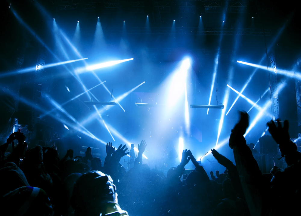 A view from the crowd looking at a stage with blue lights at a music festival
