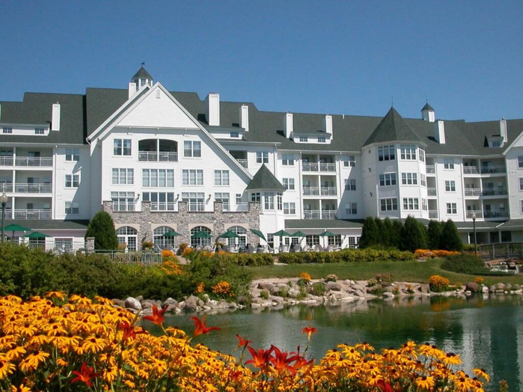A large white building that looks elegant on the side of a lake where there are yellow and red flowers, one of the best resorts in Wisconsin