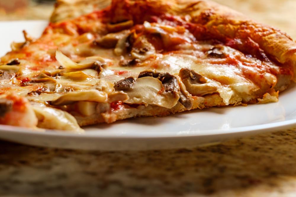 New York style cheese pizza slice with mushroom topping. There is a slice of pizza on the plate. 