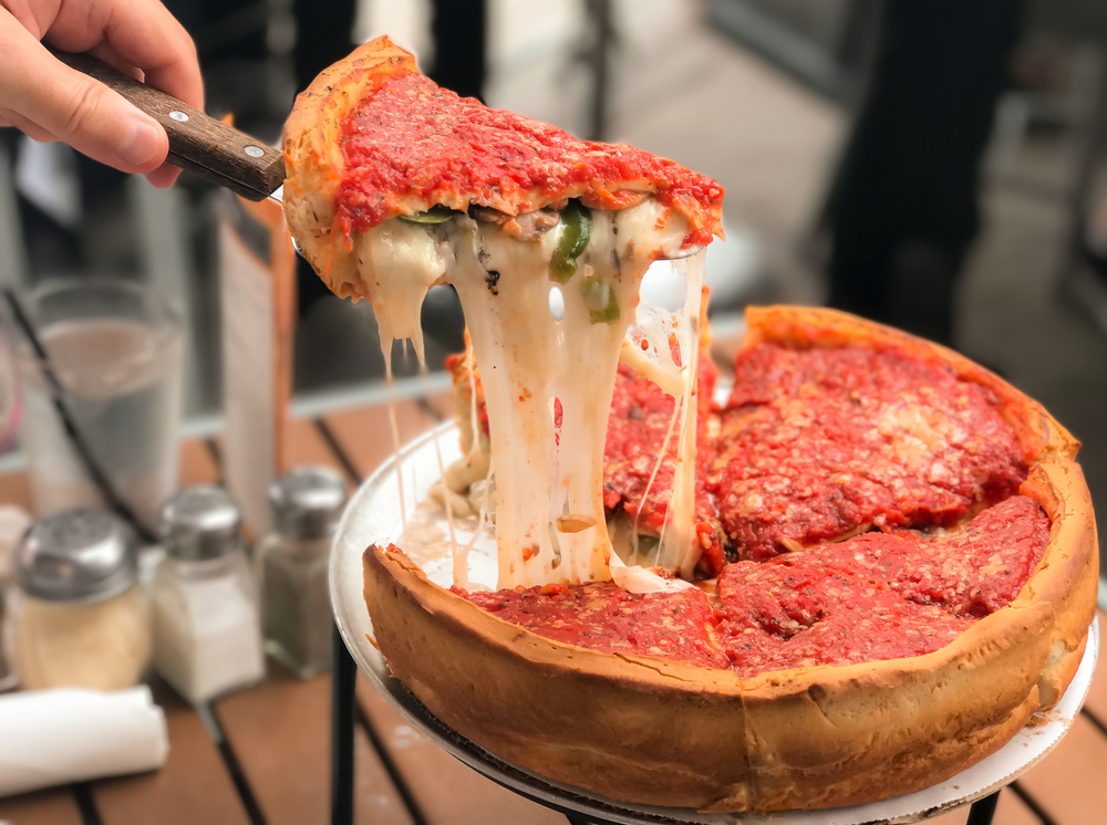 Chicago style deep dish italian cheese with tomato sauce. A piece is been lifted up out the pan.  