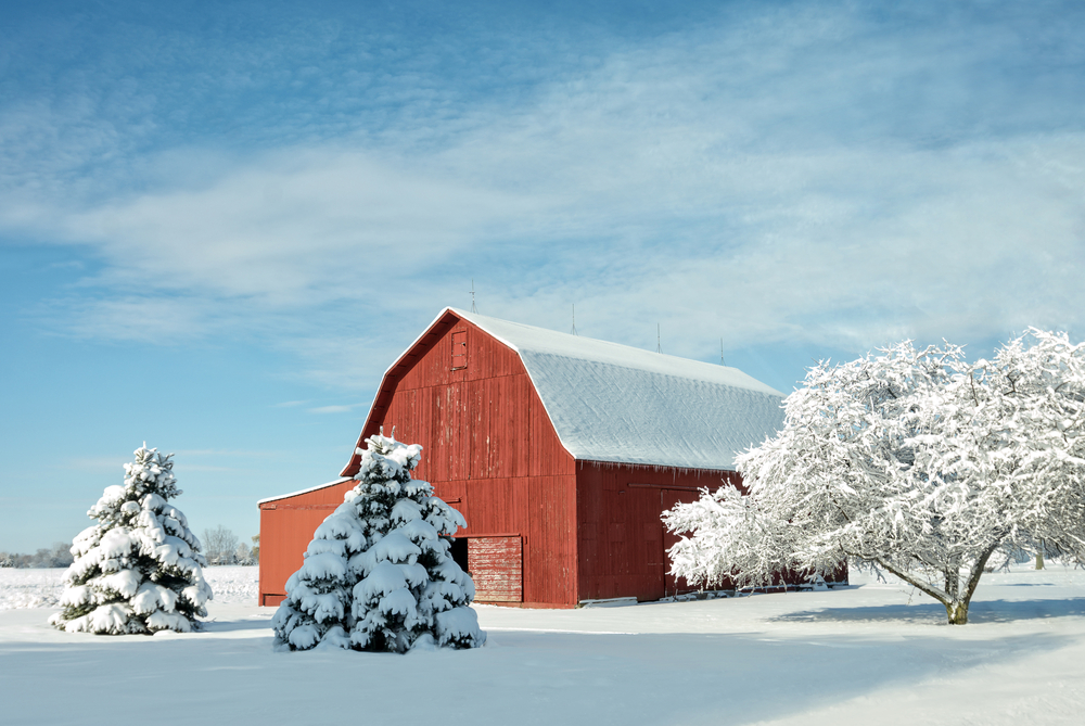 A red barn in a field with a few trees around it covered in snow on a sunny day in winter in Ohio