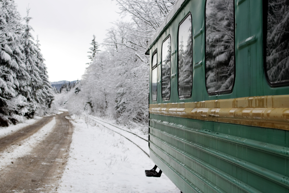 The back of a green train car going down the tracks in the woods covered in snow during winter in Ohio