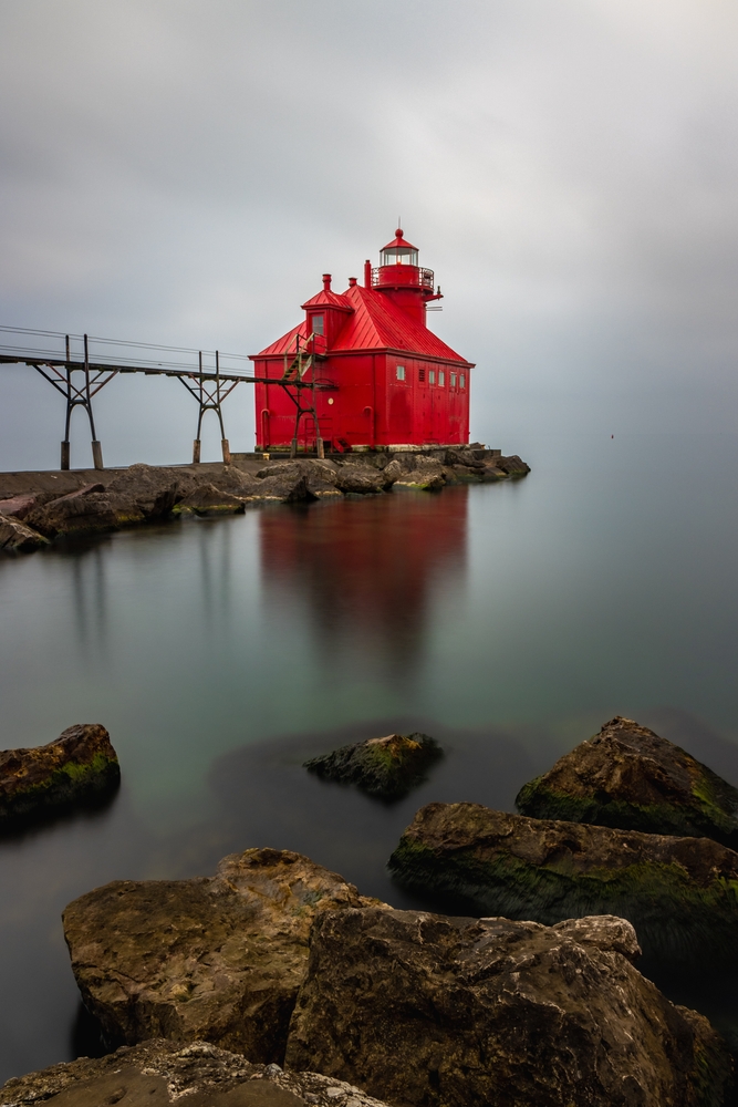 The Sturgeon Bay Ship Canal Pierhead Lighthouse in the fog. The lighthouse is red and rocks are in the foreground. 